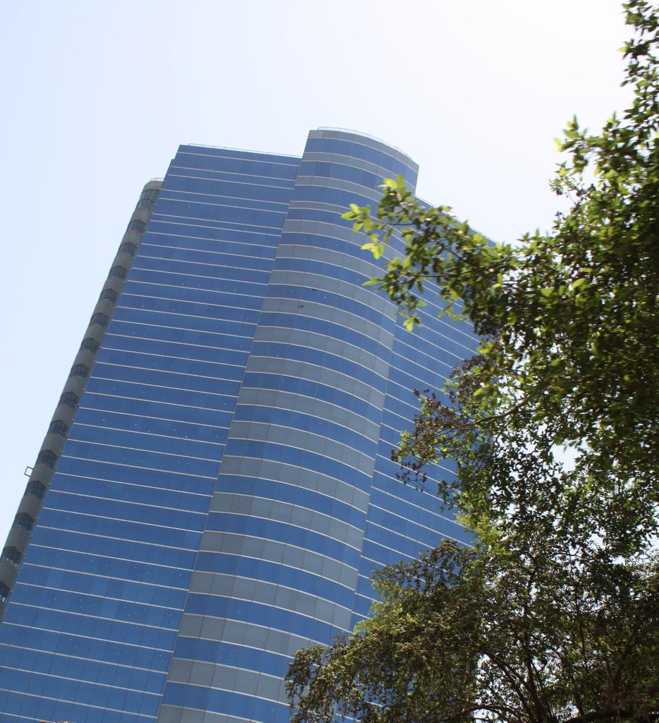 Blue glazed unitized curtain wall of Essar House rising above trees in Mahalaxmi, Mumbai